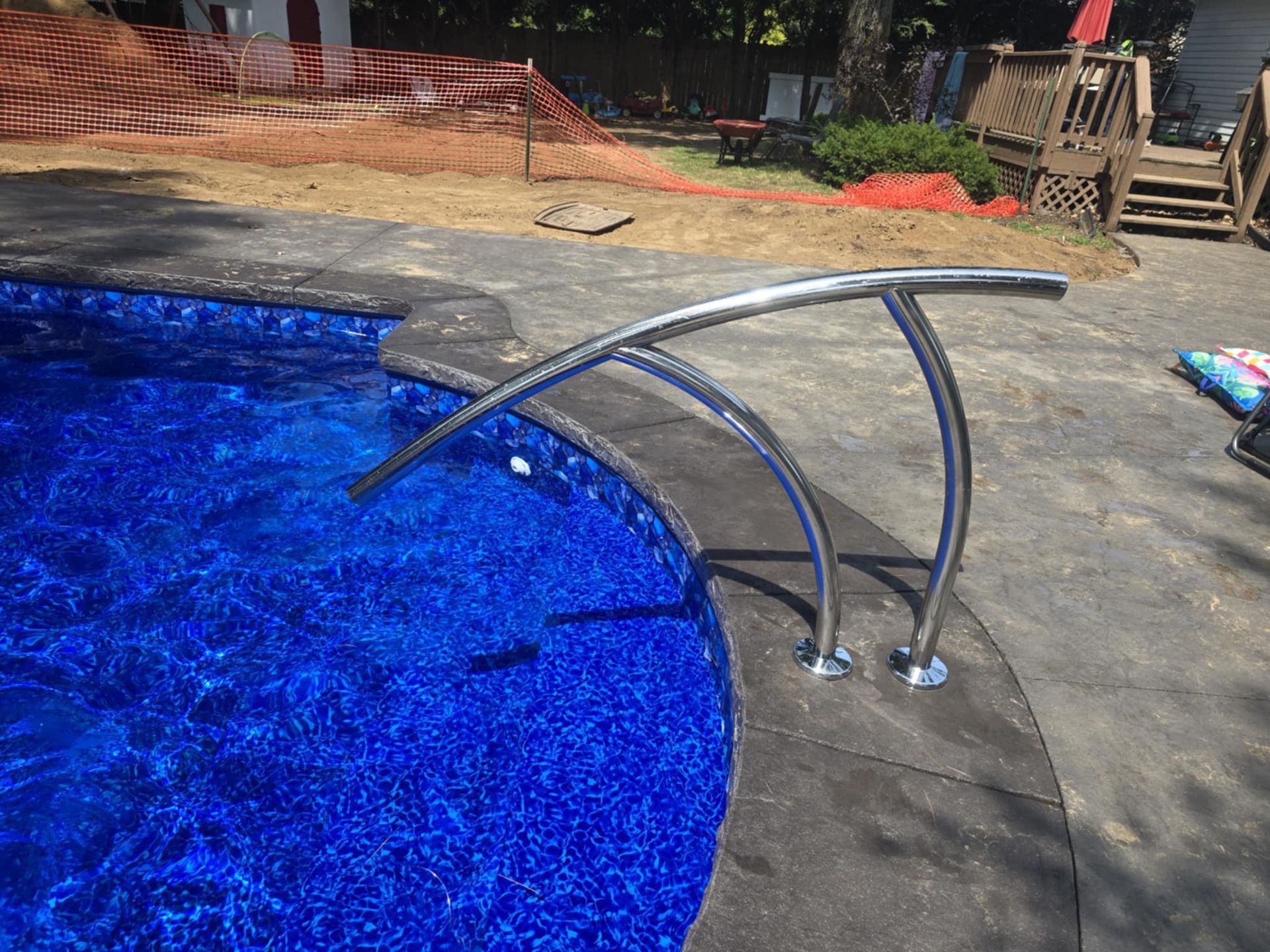 Stainless steel pool handrail over a vibrant blue water pool, with a gray textured border.