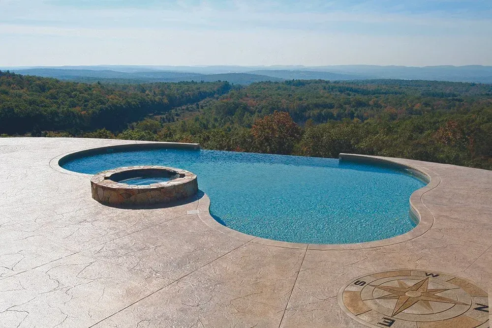 Infinity pool overlooking a scenic valley with a fire pit and compass rose.