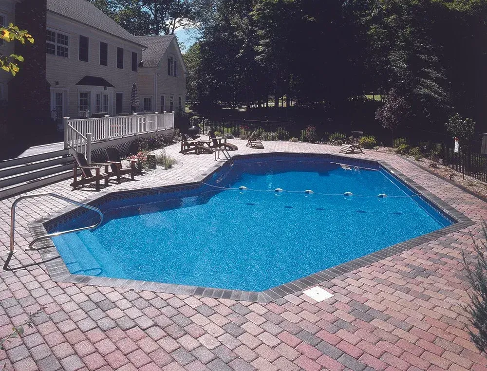 Backyard pool with brick patio, stairs, white deck, and trees.