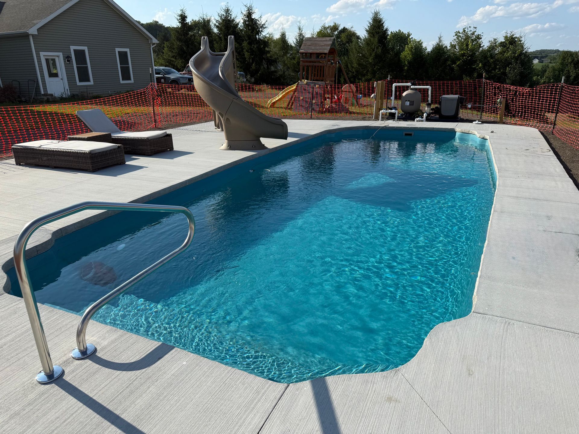 Swimming pool with blue water and stainless steel ladder; concrete deck and slide.