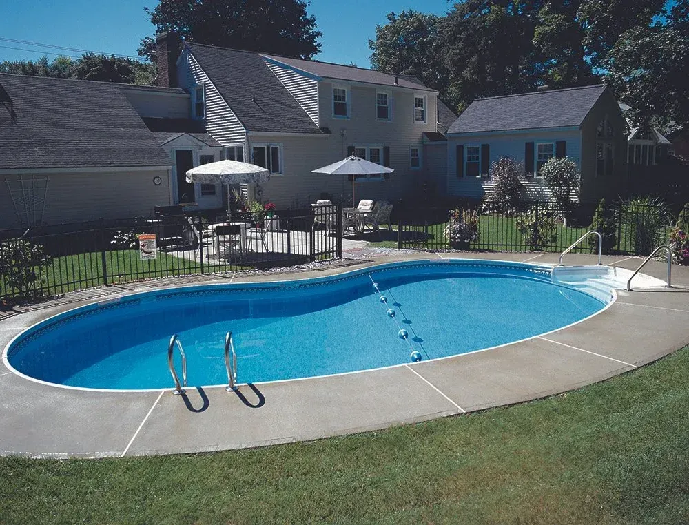 Oval-shaped swimming pool in backyard with house, patio furniture, and umbrellas.
