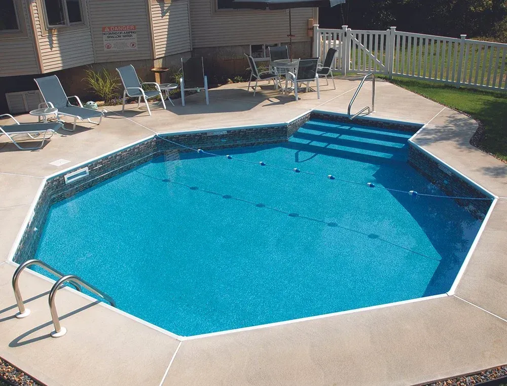 Octagonal pool with blue water and concrete surround. Steps and metal handrails.