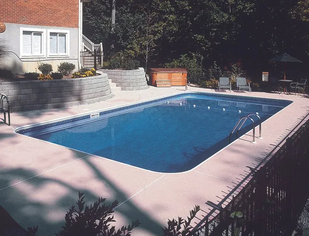 Rectangular pool with concrete patio beside a house. Spa and lounge chairs visible.