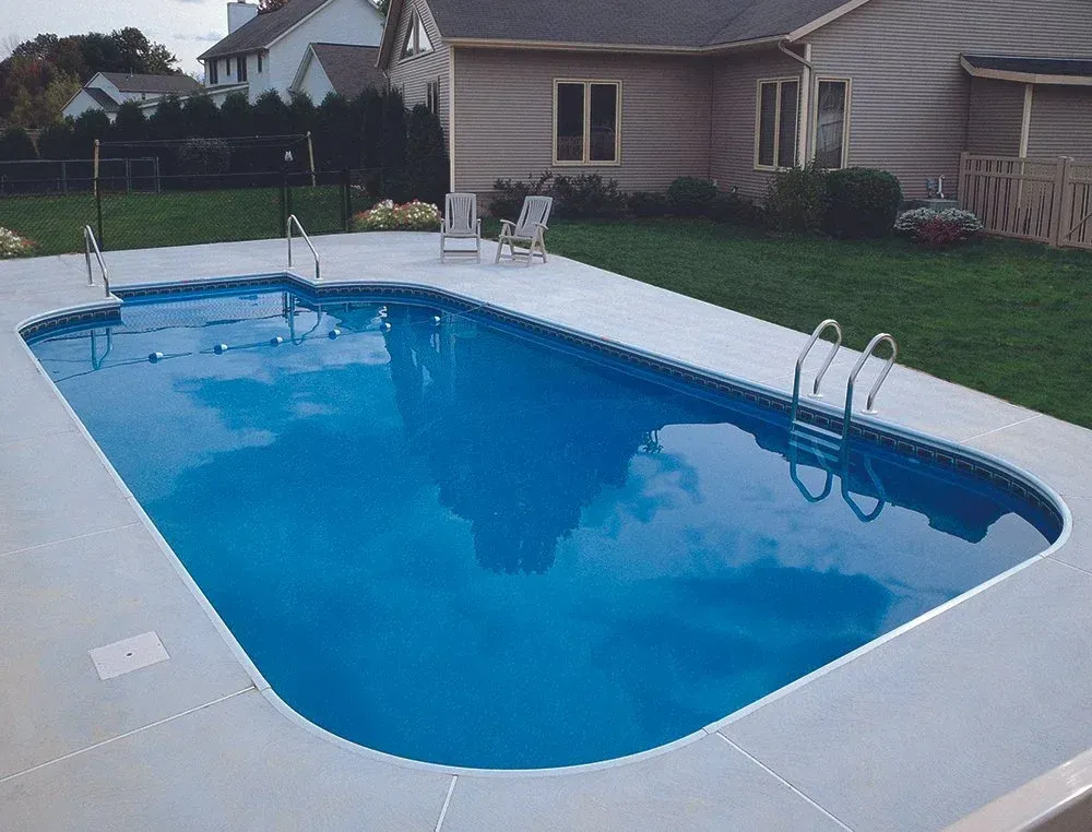 A rectangular in-ground swimming pool with blue water, concrete surround, and a grassy backyard.