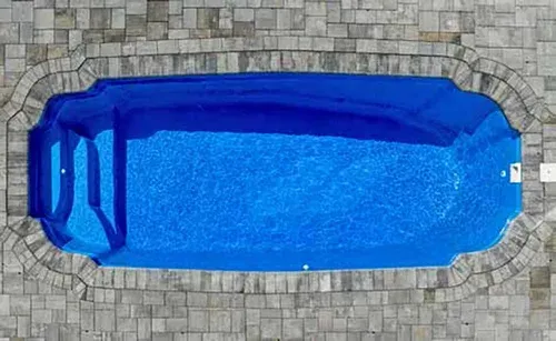 Overhead view of a blue swimming pool with a unique shape, surrounded by gray stone paving.
