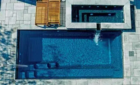 Overhead view of a rectangular pool with steps, connected to a spa and wooden pergola on stone patio.