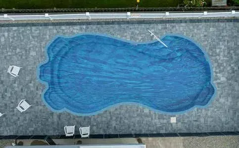 Overhead view of a blue, kidney-shaped swimming pool surrounded by gray stone tiles; four white lounge chairs on the side.