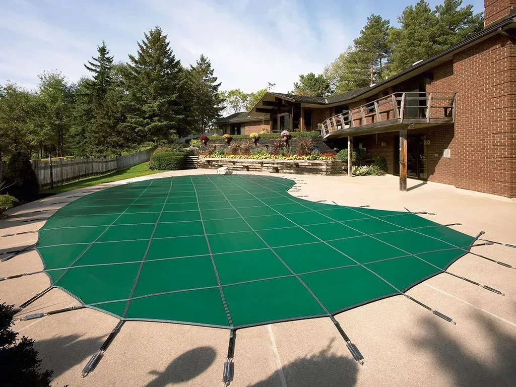 Green pool cover on a concrete patio next to a house with a deck.