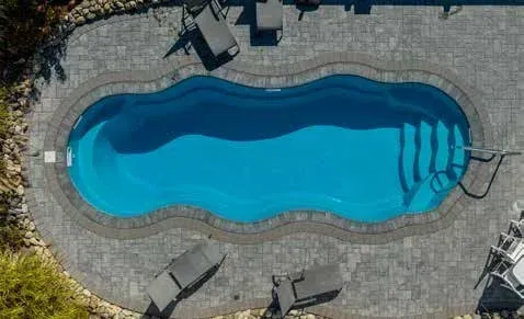 Overhead view of an irregularly shaped swimming pool with blue water, surrounded by grey pavers and lounge chairs.