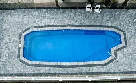 Overhead view of a blue swimming pool with gray stone border and two white lounge chairs.