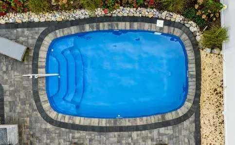Overhead view of a blue-covered pool surrounded by stone and landscaping.