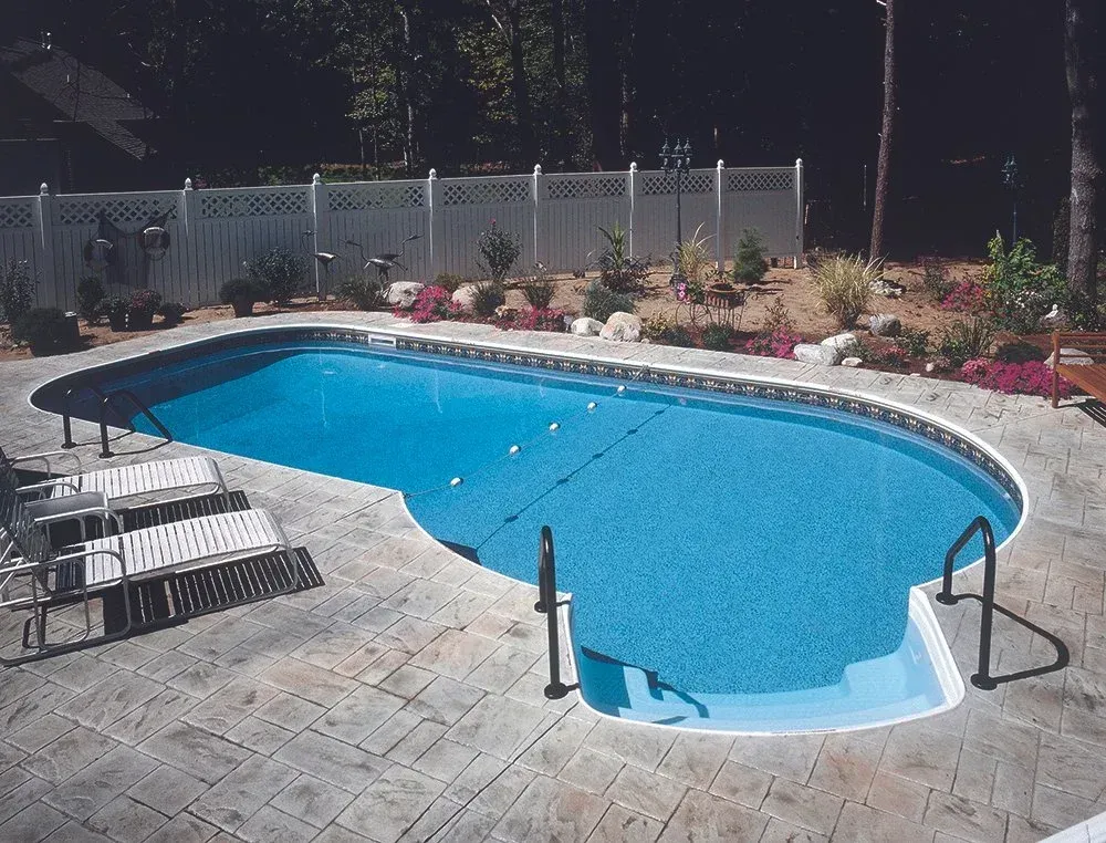 Pool with blue water and gray concrete patio, surrounded by a white fence and landscaping.