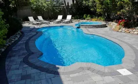 Blue swimming pool with connected jacuzzi, surrounded by patio and lounge chairs.