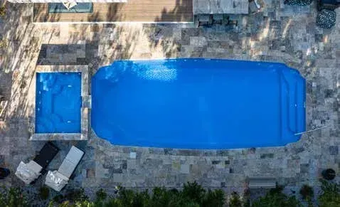 Overhead view of two blue pools, a rectangular pool and a smaller square hot tub on a stone patio.