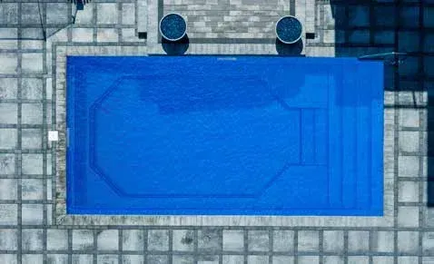 Overhead view of a rectangular blue swimming pool with steps, surrounded by stone paving.