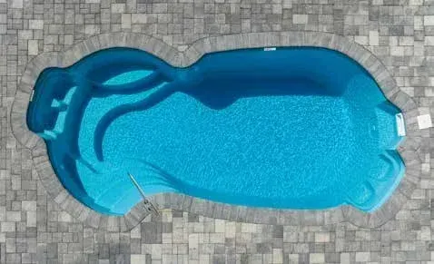 Overhead view of a blue, kidney-shaped swimming pool surrounded by gray paving stones.