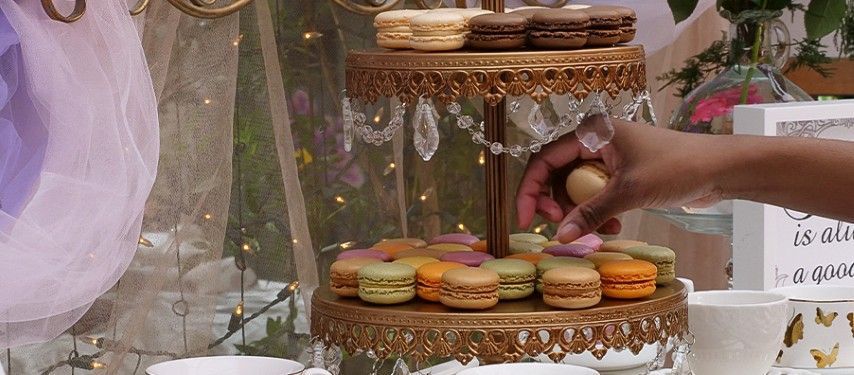 A person is putting a macaroon on top of a cake stand.