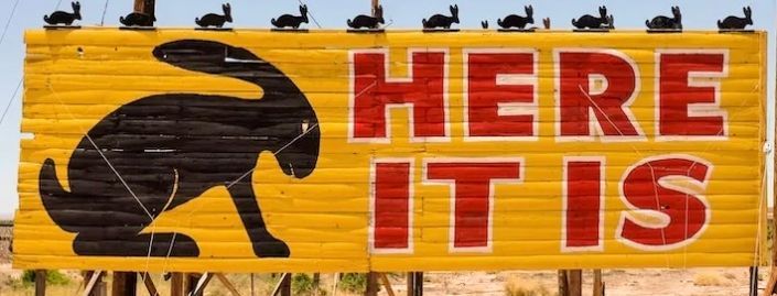 A yellow sign with a rabbit and the words here it is