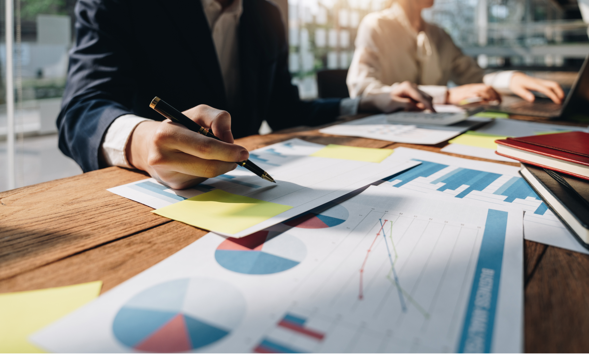 A man is writing on a piece of paper while sitting at a table with other people.