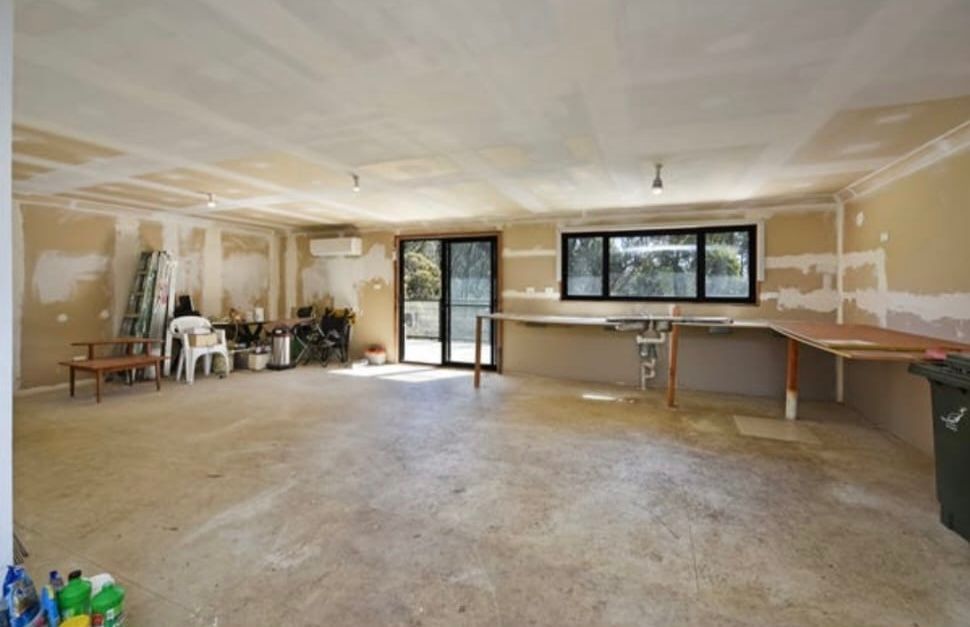 An unfinished, spacious interior room with concrete flooring, unpainted drywall, a large window, and sliding glass doors.