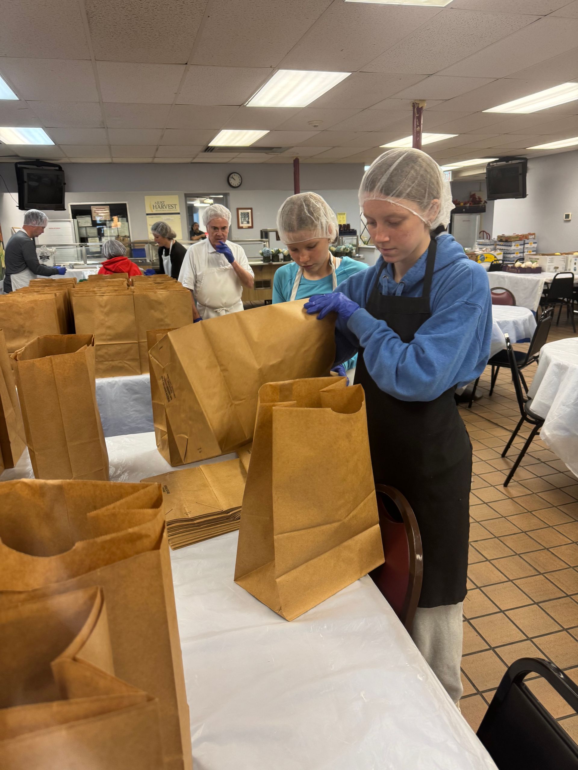 A group of people are working in a kitchen preparing food in paper bags.