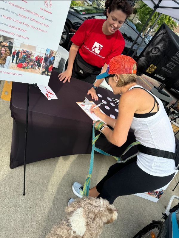 A woman in a red shirt is signing a form with a dog