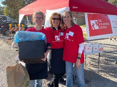 Three women in red shirts are standing in front of a tent holding boxes.