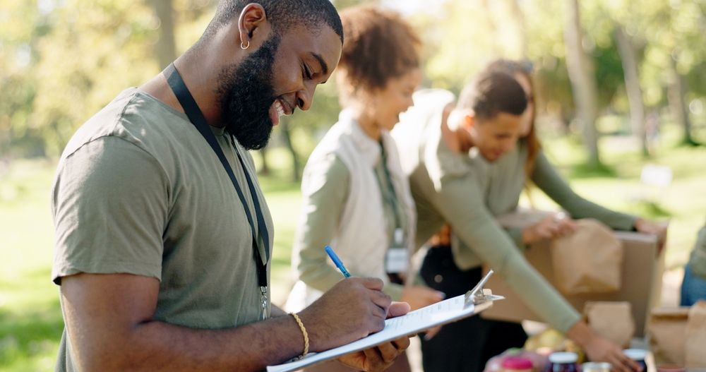 A man is writing on a clipboard in front of a group of people.