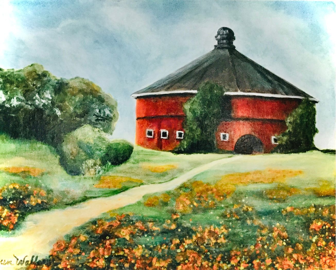 Red round barn on a grassy hill, surrounded by trees and a path, under a cloudy sky.