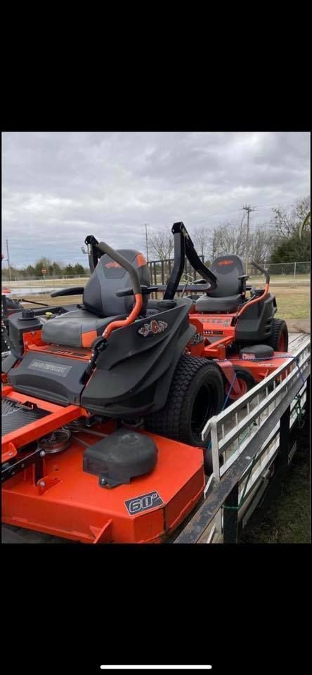 A row of orange and black lawn mowers are parked on a trailer.