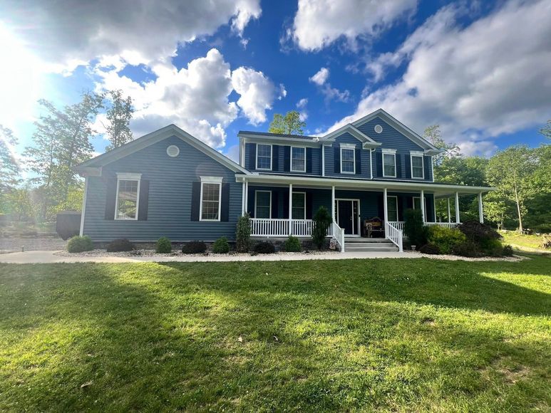 Blue two-story house with a porch, under a partly cloudy sky, with green grass in the foreground.