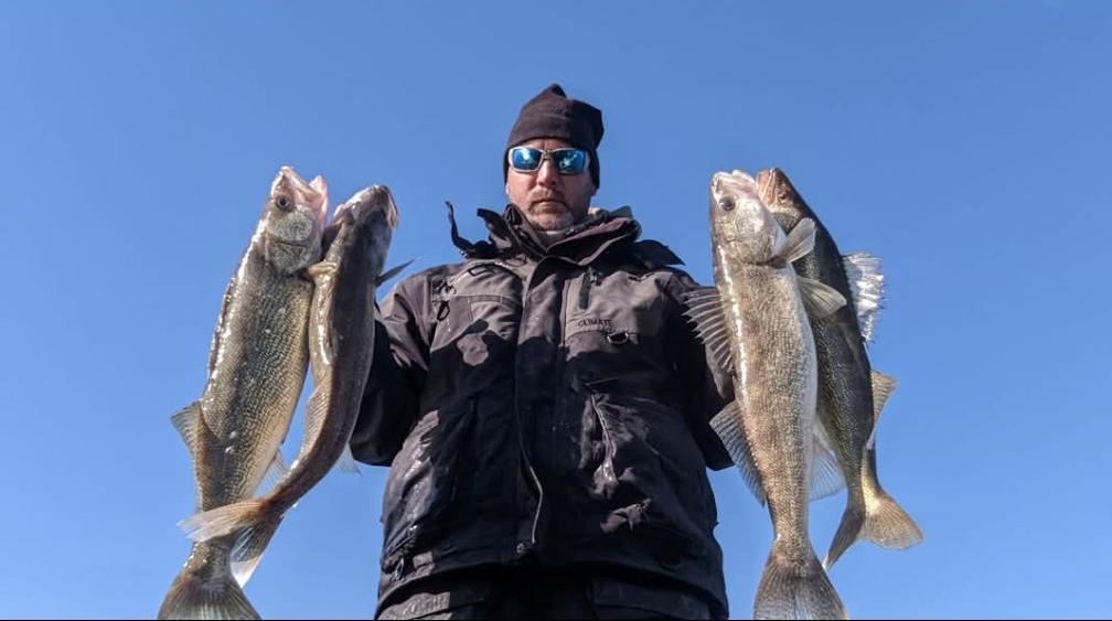Person holding two large fish against a clear blue sky
