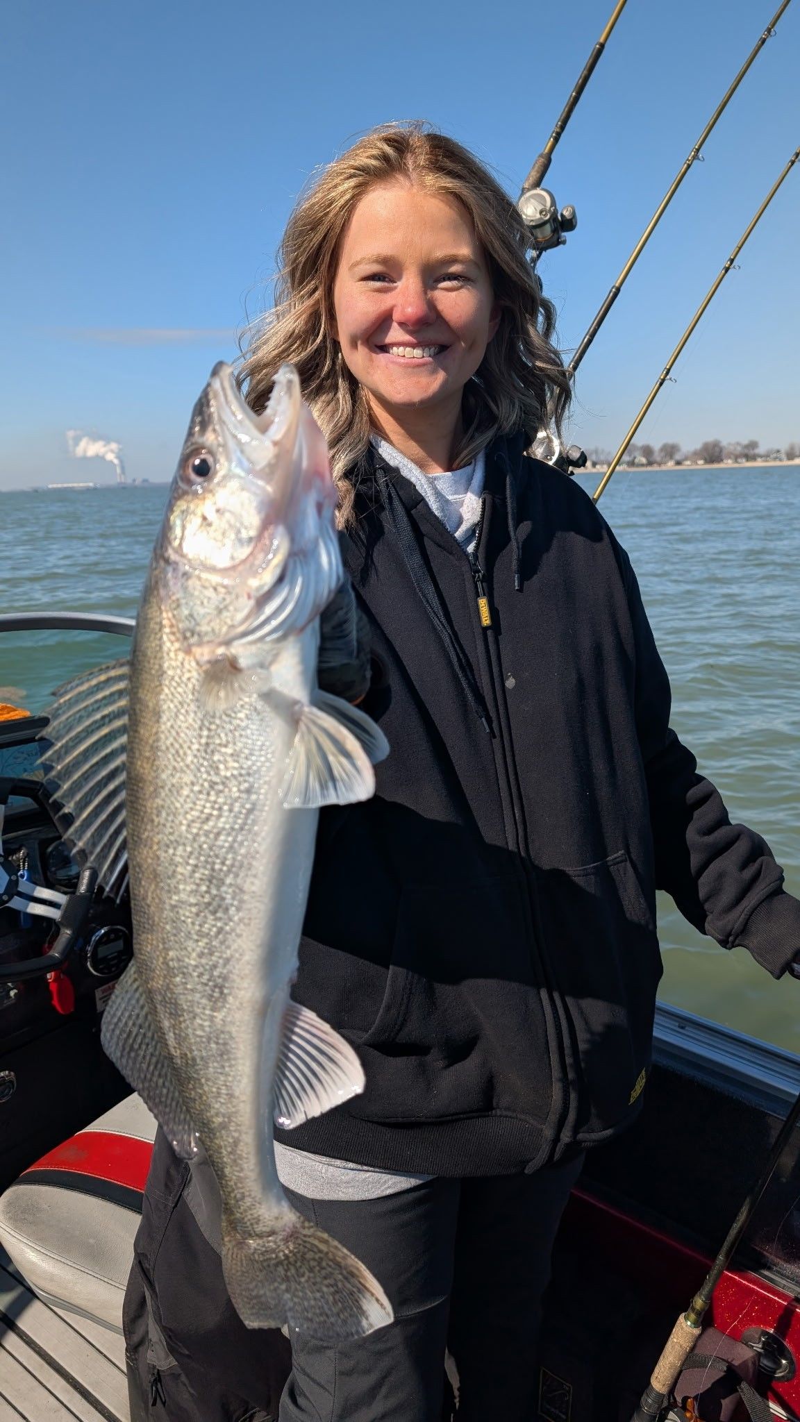 Woman on a boat holding a large silver fish, smiling on the water under a clear sky.