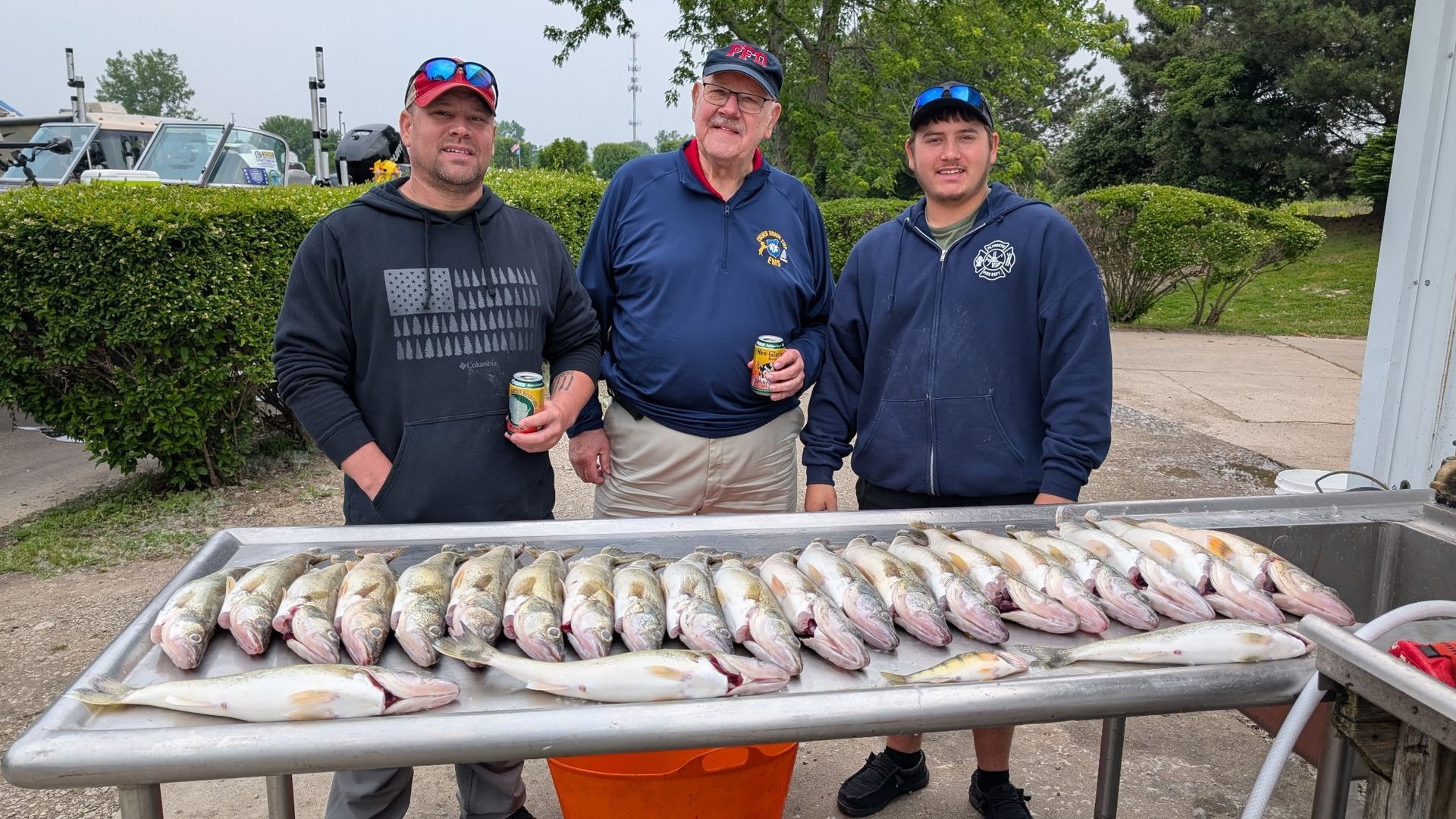 Three people stand behind a table of freshly caught fish outdoors, smiling at the camera.