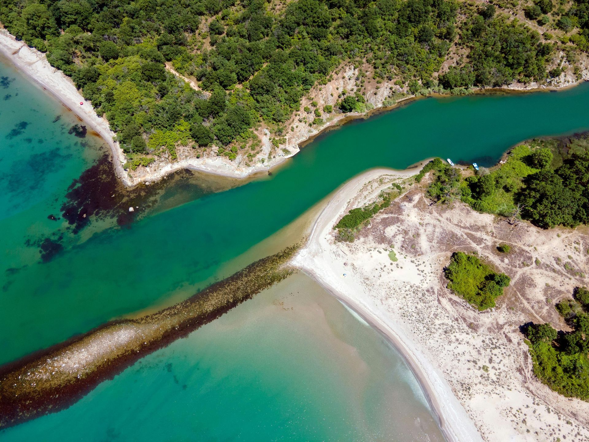 Aerial view of turquoise river meeting the sea beside sandy shores and green cliffs
