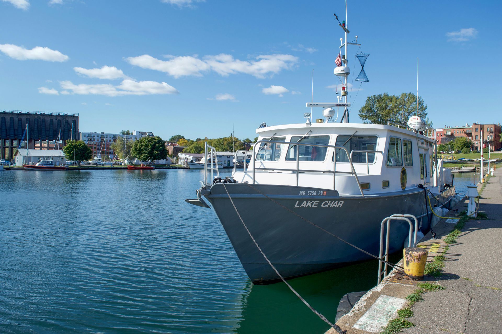 Gray boat docked at a sunny harbor with blue water and buildings in the background