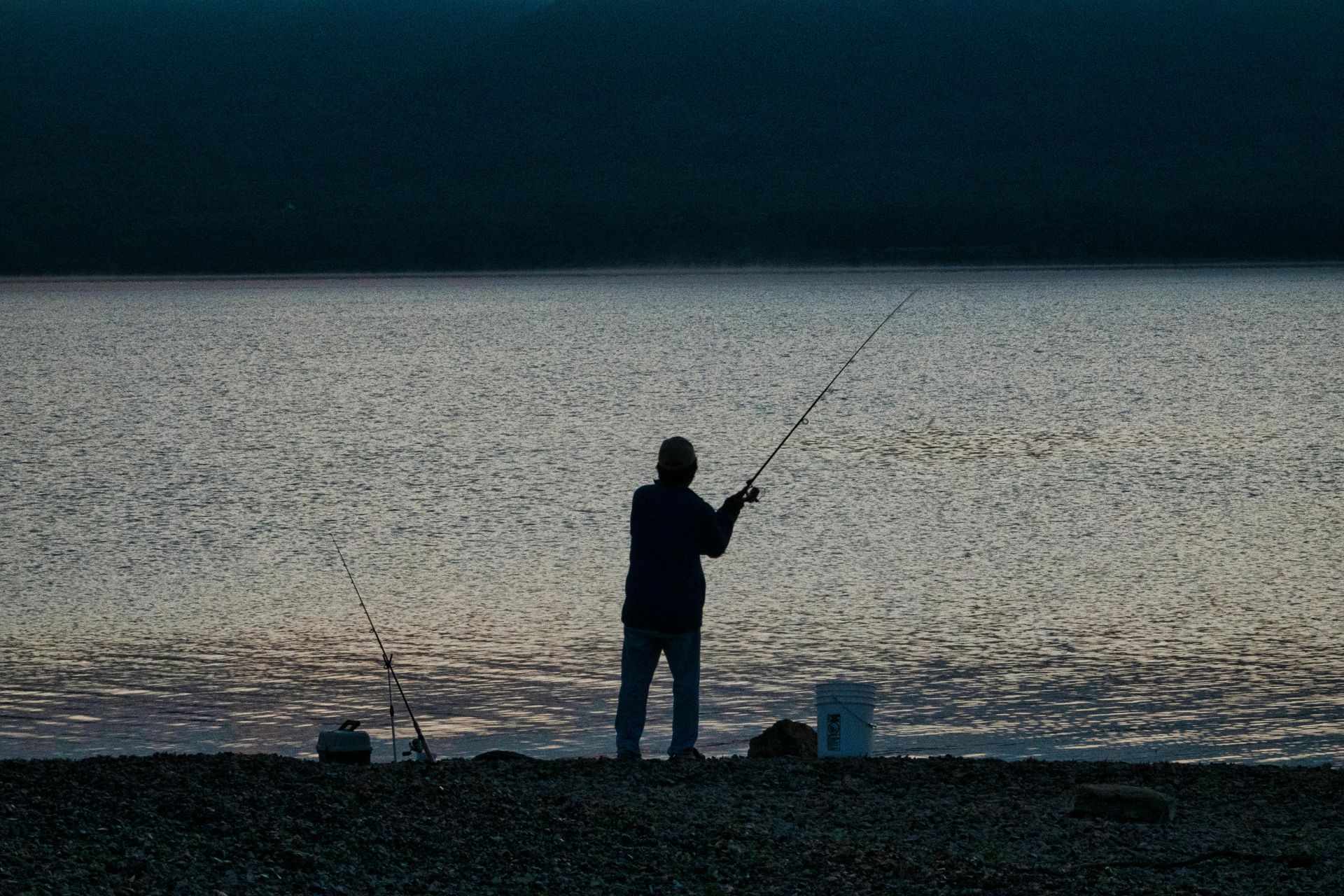 Person fishing at dusk beside a calm, shimmering body of water