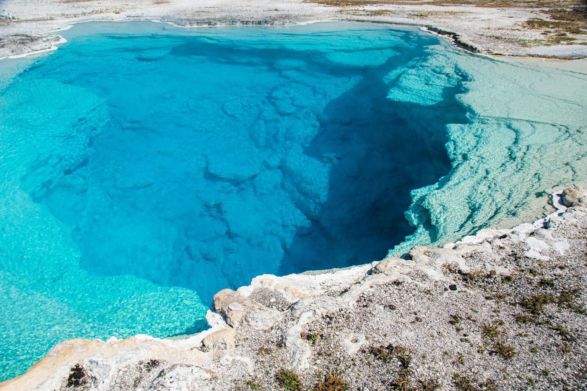 Bright turquoise hot spring with a rocky white shoreline and deep blue center