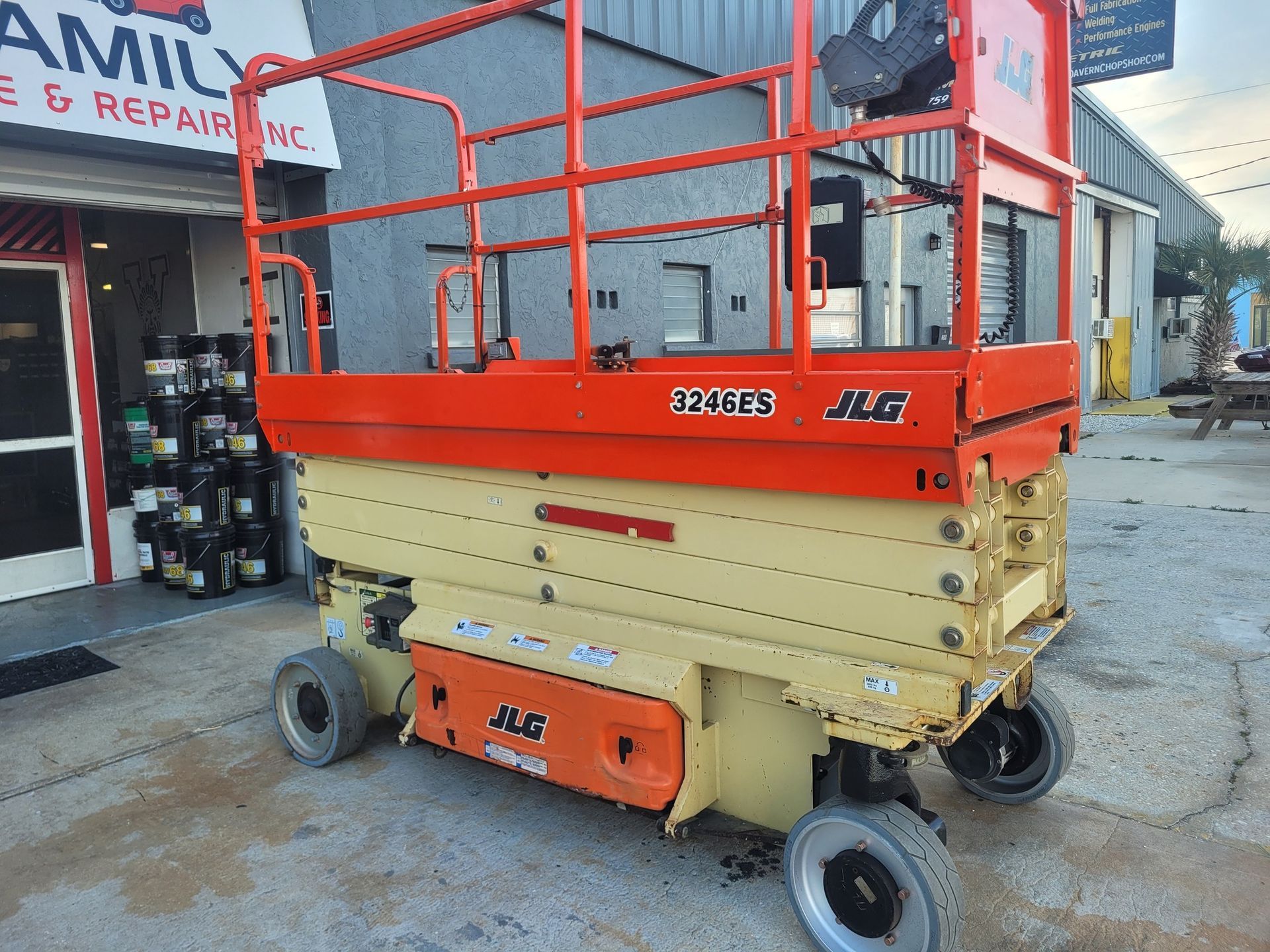 Orange and beige JLG scissor lift parked in front of a repair shop.