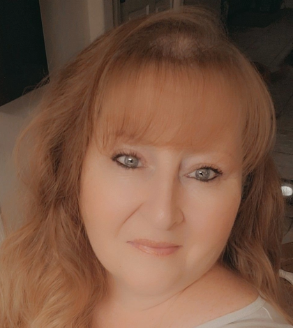 Woman with light-colored hair, bangs, and blue eyes, looking towards the camera.