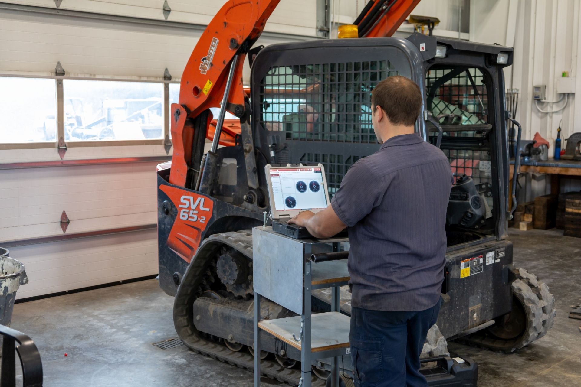 Man using a computer to diagnose a compact track loader in a workshop.