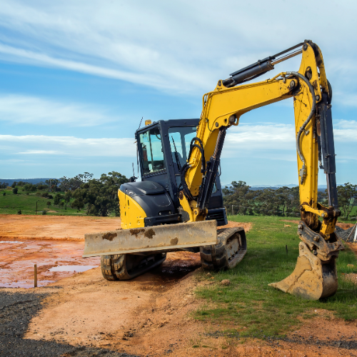 Yellow excavator on dirt and grass, blue sky in background.