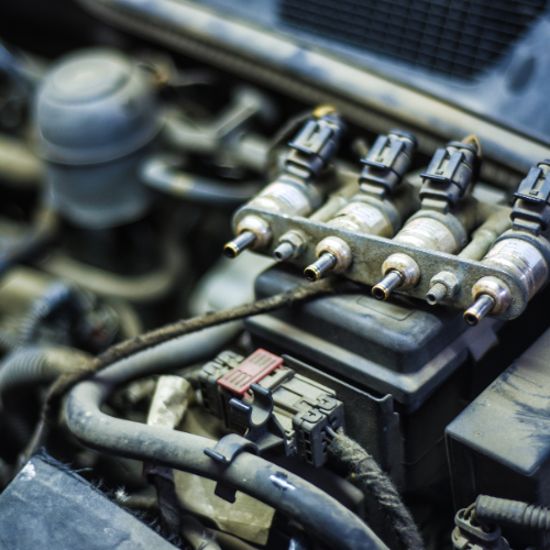 Close-up of a dirty car engine, focusing on the fuel injectors and associated wiring.