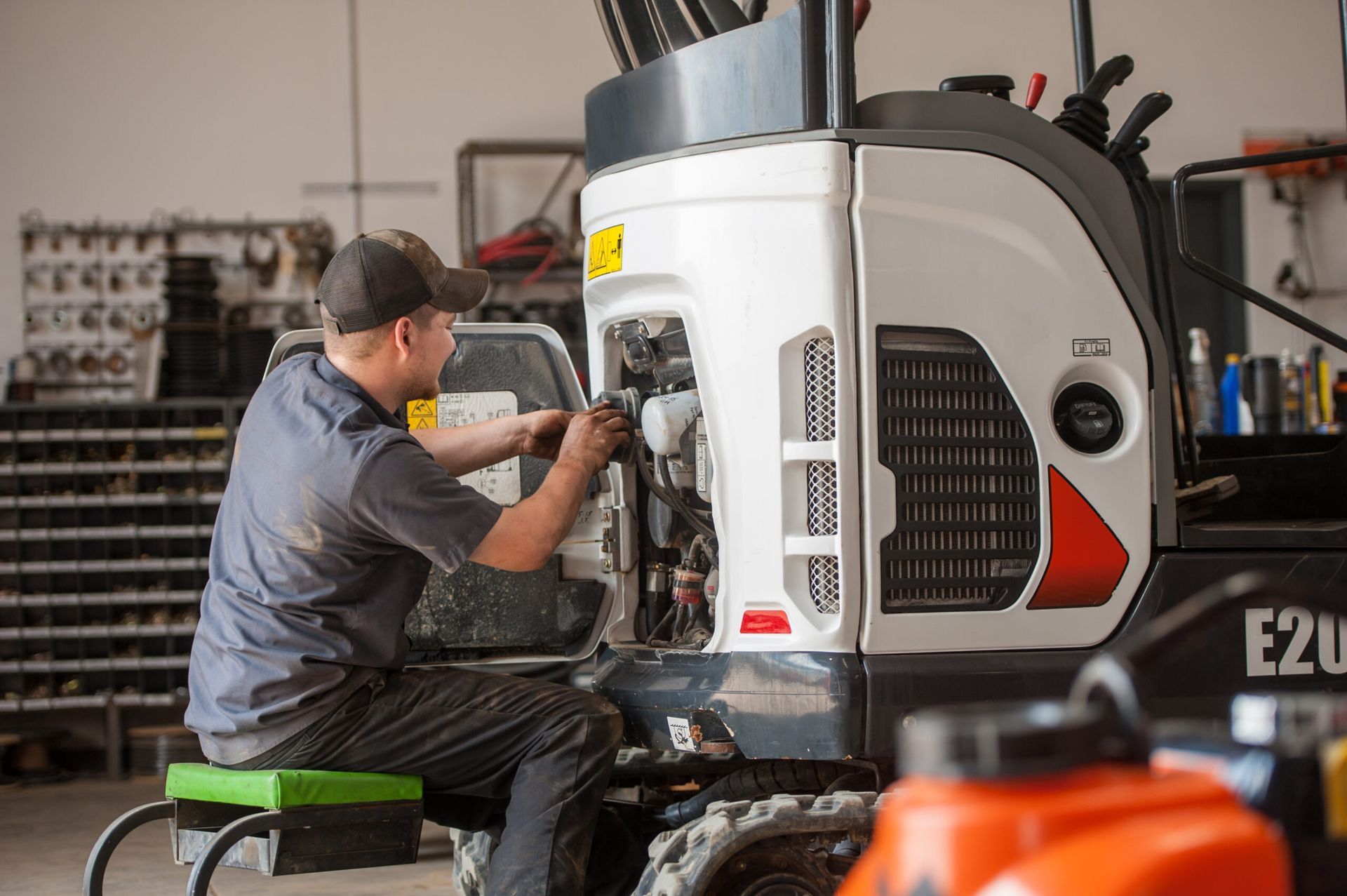 Mechanic working on a white and black Bobcat excavator in a shop.