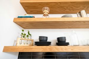 A wooden shelf with plates , bowls , and a vase on it.