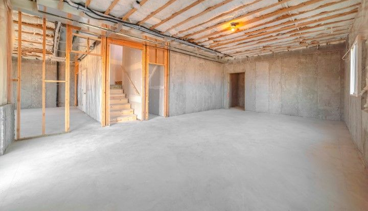 An unfinished basement with concrete walls, exposed ceiling joists, a wooden staircase, and a concrete floor.