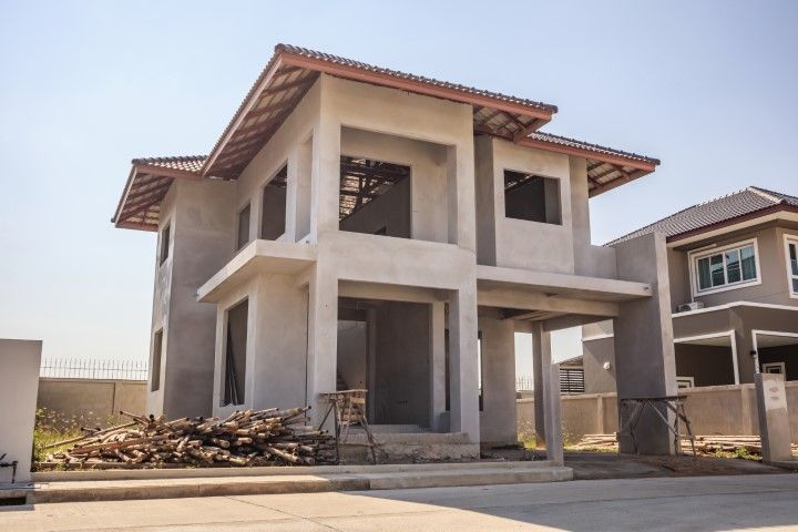 An unfinished two-story concrete house under construction with tiled roofing, located in a residential area.