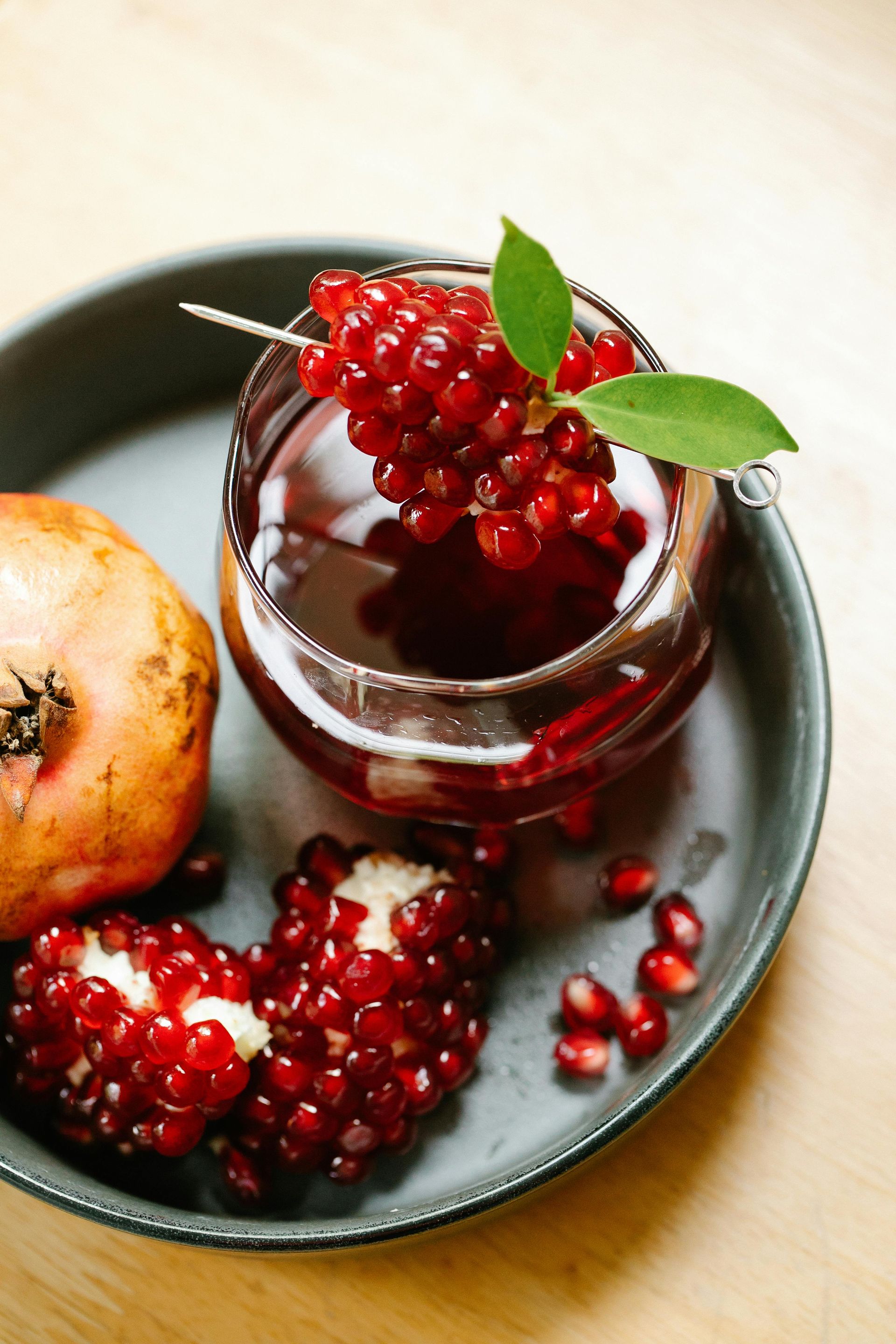 A glass of pomegranate juice next to a pomegranate on a plate.