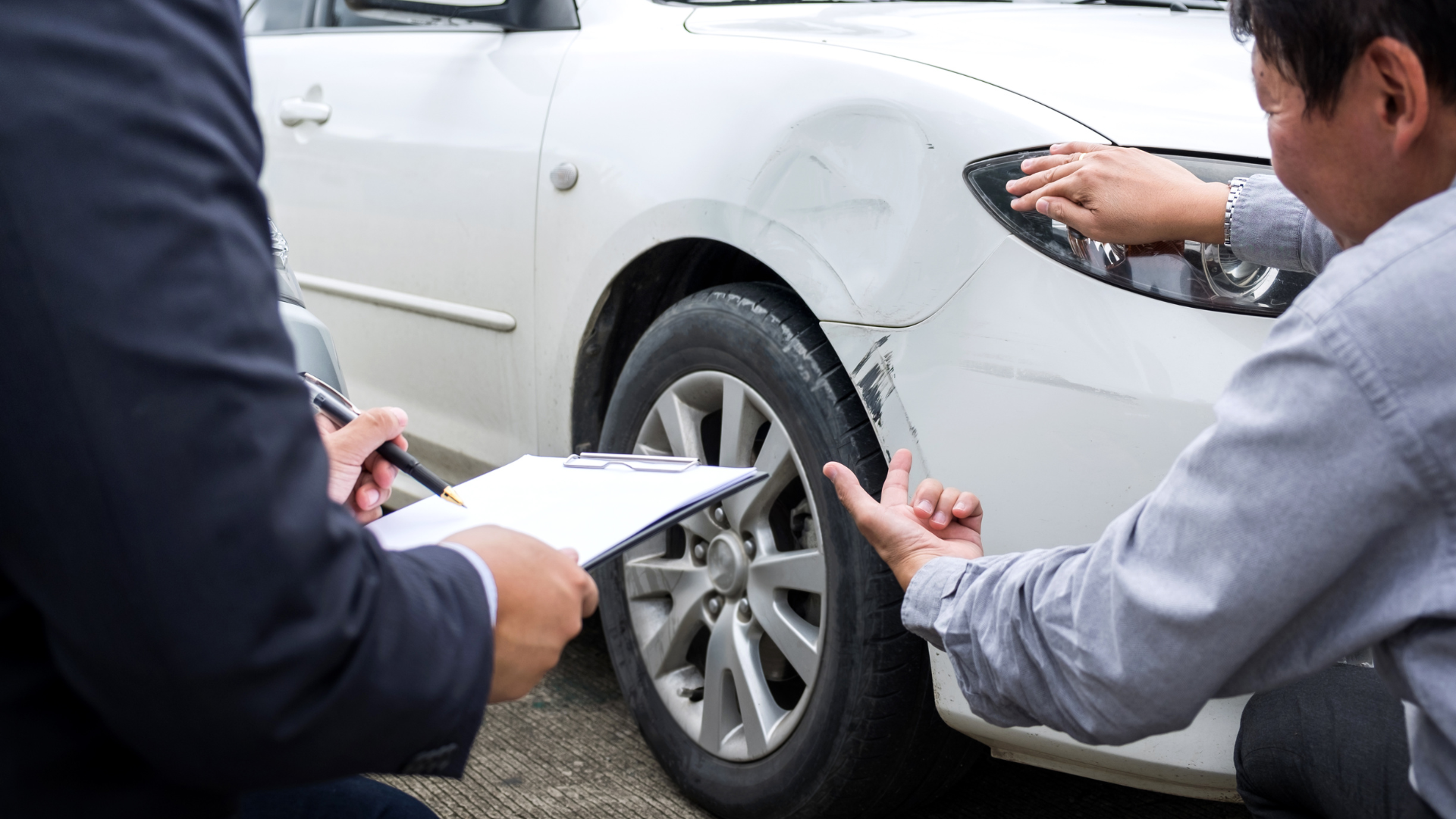 Two men are looking at a white car with a damaged bumper.