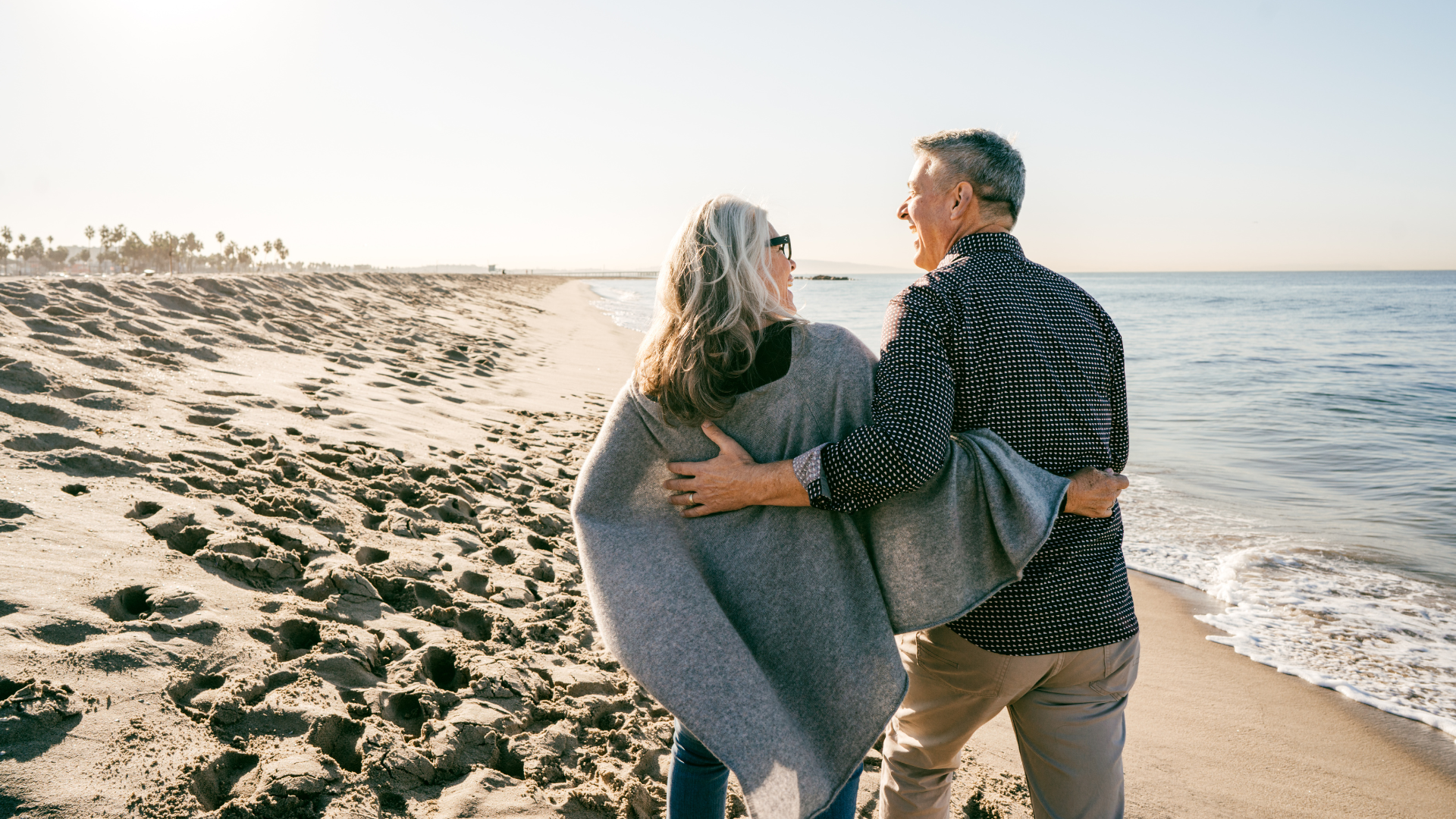 A man and a woman are standing on a beach looking at the ocean.